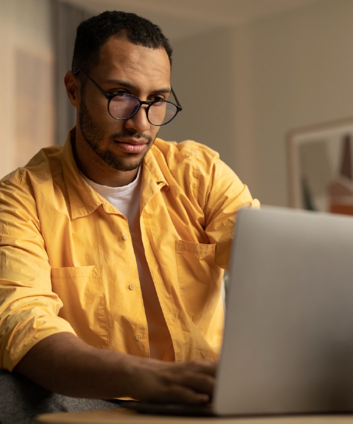 A man in a yellow shirt looks worriedly at his laptop because it appears to be infected with spyware.