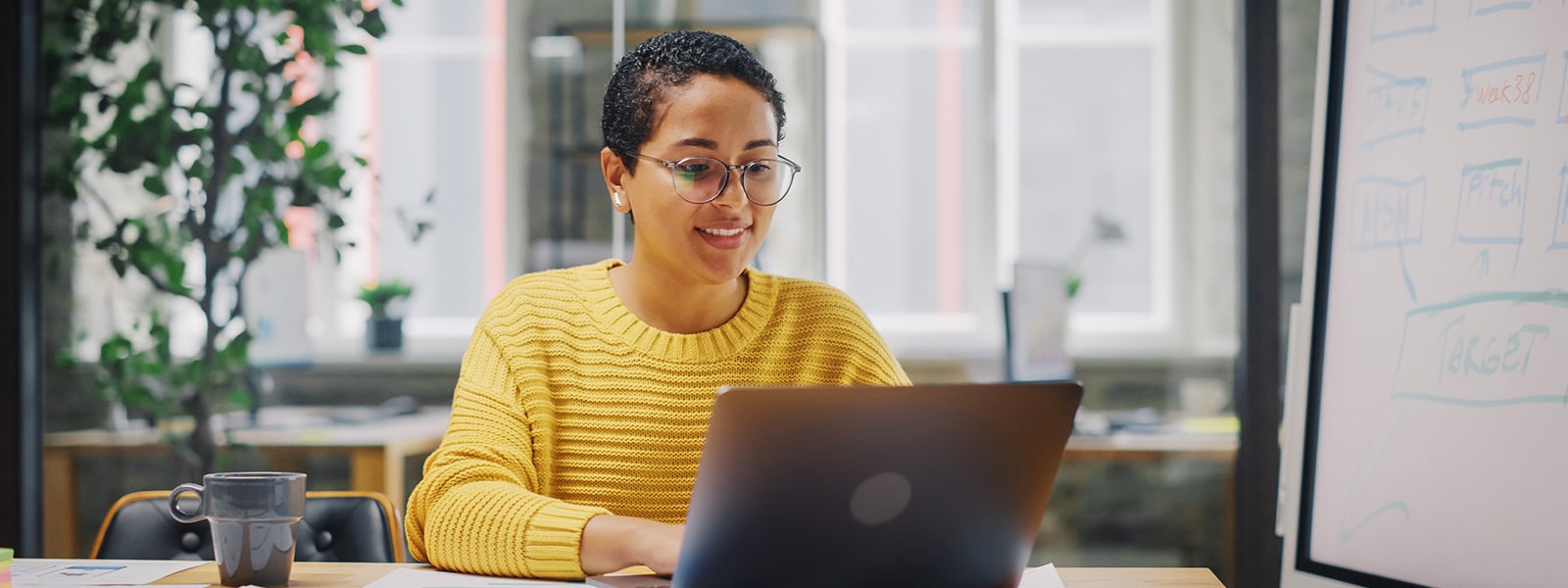 A woman in a yellow sweater looking up the answer to what is antivirus software on a laptop.