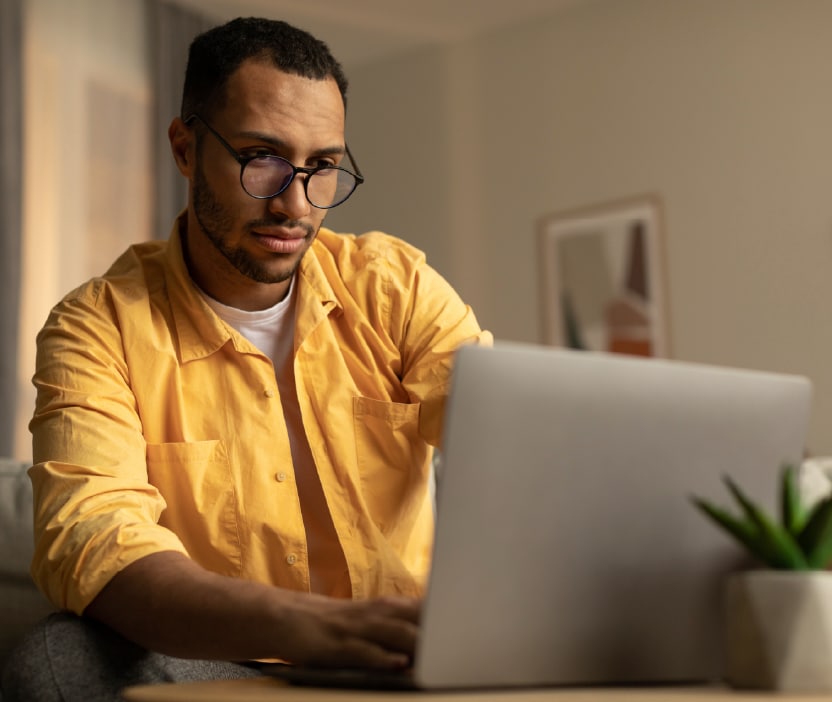 A man in a yellow shirt looks worriedly at his laptop because it appears to be infected with spyware.