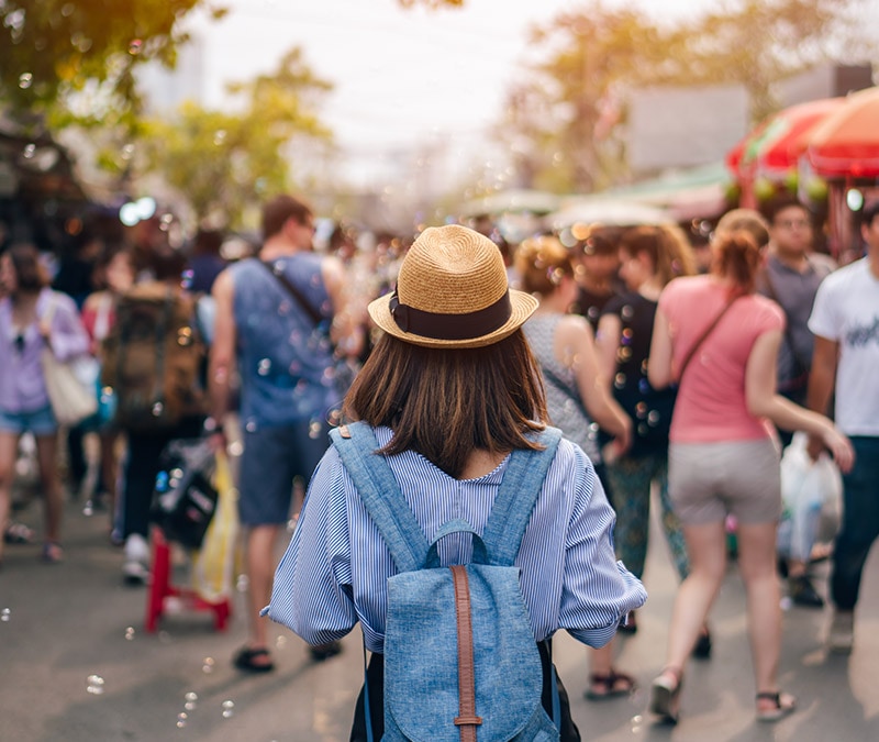A woman wearing a straw hat and backpack browses a busy outdoor market, symbolizing caution against Facebook Marketplace scams.
