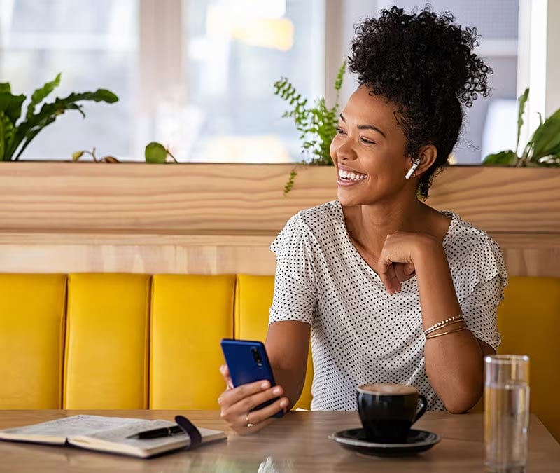 A smiling woman on her iPhone in a cafe after learning how to use a VPN on an iPhone to stay safe.