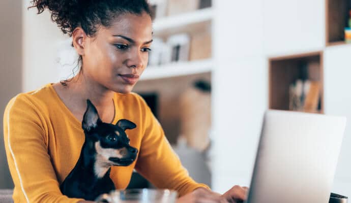 Woman using laptop while dog sits on her lap